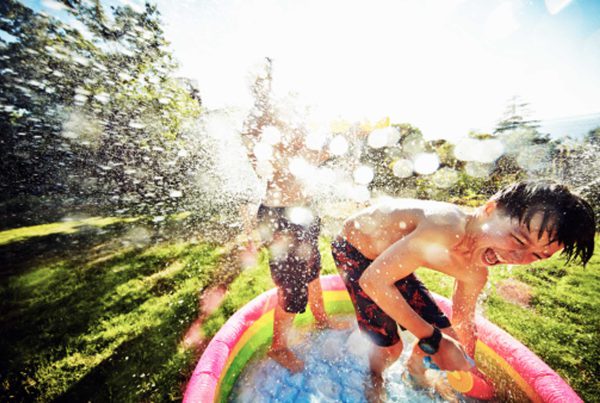 Boys standing in a baby pool laughing and spashing each other with water.