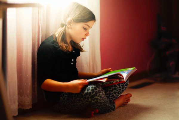 A girl in pigtails sits on the floor and reads a book.