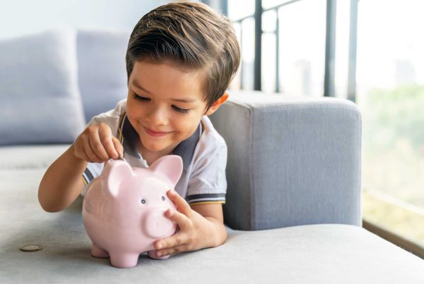 A young boy smiles as he puts money into his pink ceramic piggy bank. 