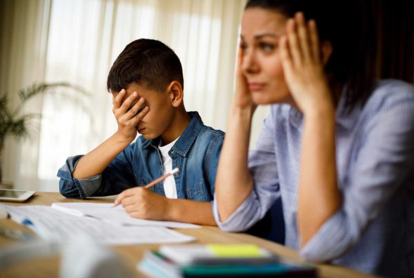A Hispanic mom shows frustration at helping with homework while her grade school son hides his face.