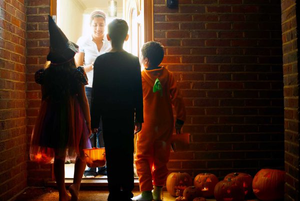 Three kids in costumes are at a front door waiting for the homeowner to hand out candy.