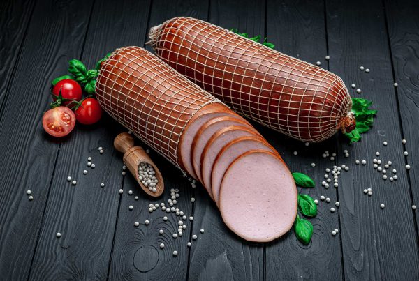 Two bologna sausages displayed neatly on a wood table with salt, tomatoes, and basil garnishes.