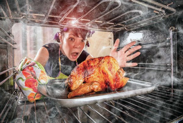 A Caucasian young woman in pigtails pulls a burning turkey out of an oven fill with smoke.
