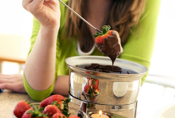 A woman pulls a strawberry from a double-boiler filled will chocolate fondue.