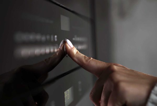 Close up on a left hand with the forefinger pressing a button on a microwave.